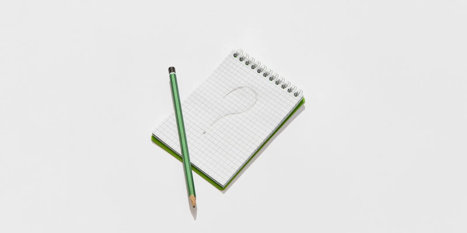 A question mark drawn in a notebook beside a green pencil